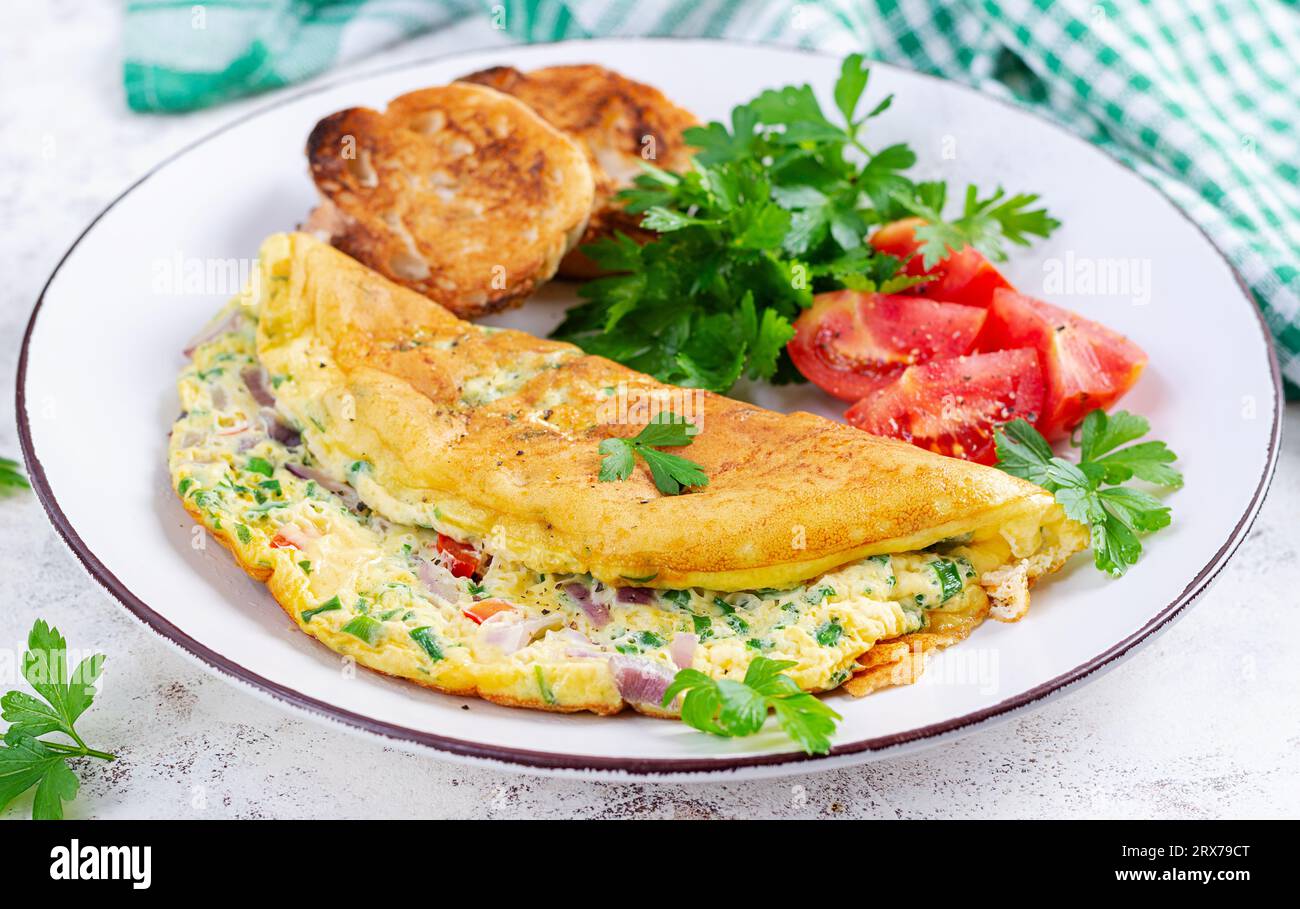 Omelette con pomodori, formaggio e cipolla rossa su piatto bianco. Frittata - omelette italiane. Foto Stock
