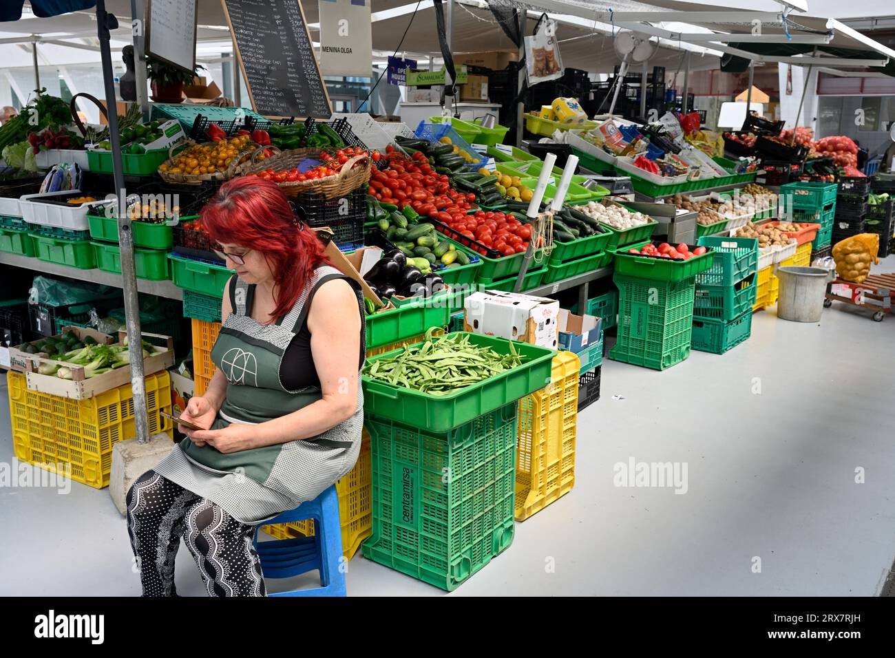 Donna che lavora in bancarelle di frutta e verdura al mercato municipale che guarda uno smartphone, Mercado Municipal de Matosinhos, Porto, Portogallo Foto Stock