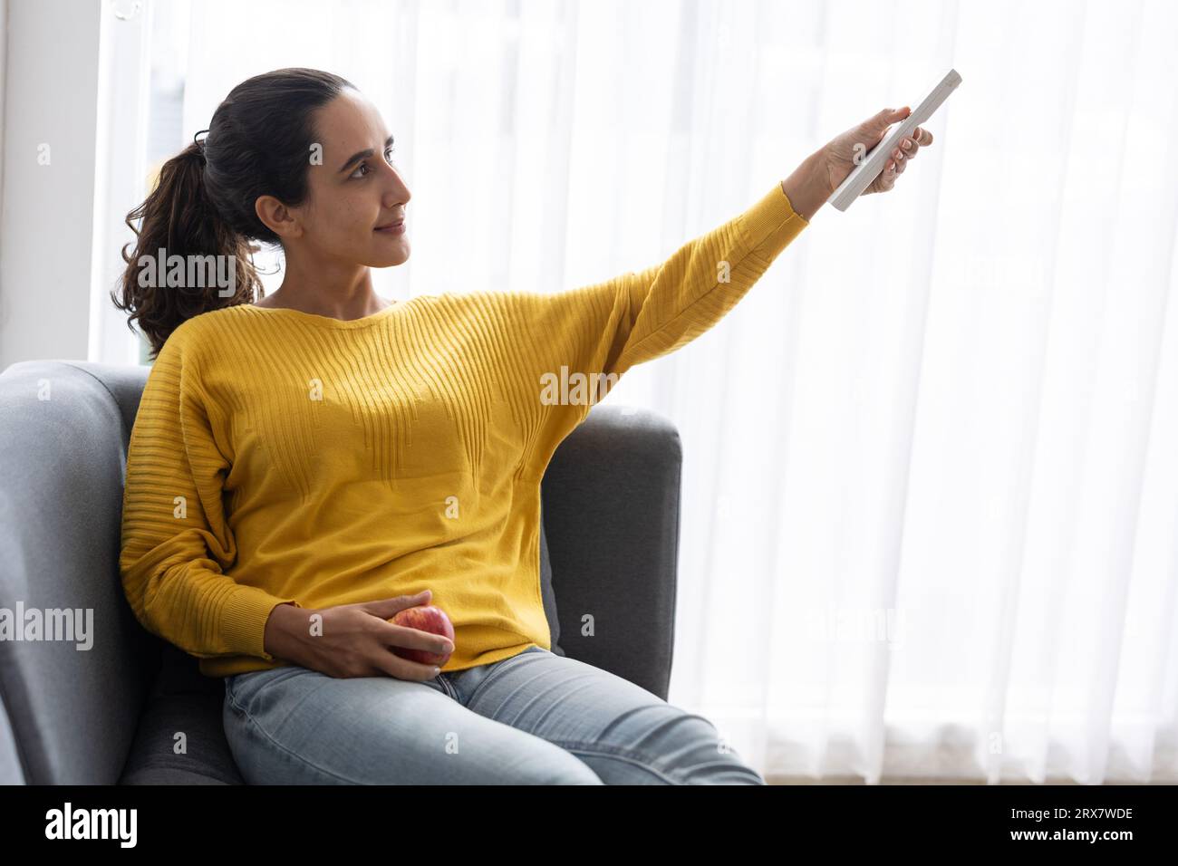 Donna indiana ispanica che utilizza il telecomando dell'aria condizionata, modifica la temperatura della stanza per un soggiorno confortevole in casa durante la stagione estiva Foto Stock