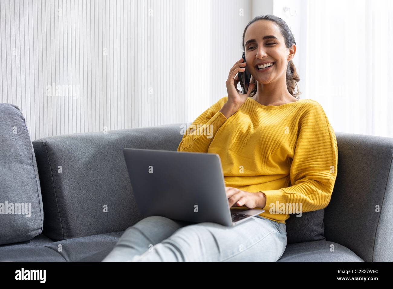 Adolescente universitaria o donna d'affari indiana ispanica seduta rilassarsi sul divano felice di divertirsi con i dispositivi tecnologici moderni che lavorano a casa Foto Stock