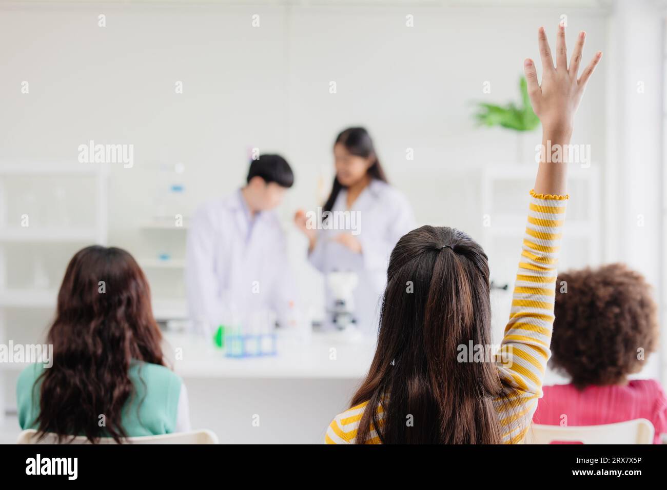 Gli studenti intelligenti che alzano la mano hanno una domanda per il gioco di ruolo degli scienziati nella moderna classe scolastica di scienza Foto Stock