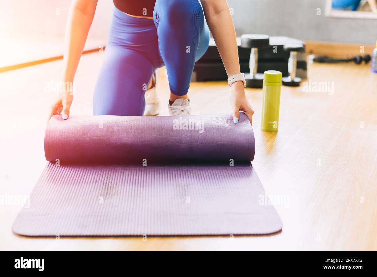 Closeup fitness Woman nello studio del club sportivo con tappetino yoga. Una giovane donna allenta il tappeto pilates in un corso di fitness. Foto Stock