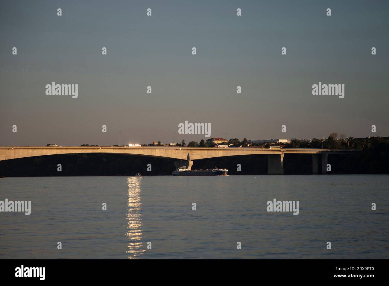 Belgrado, Serbia, 2 settembre 2023: Una chiatta fluviale che naviga lungo il Danubio a monte passa sotto il Ponte Pupin (Pupinov Most) al tramonto Foto Stock