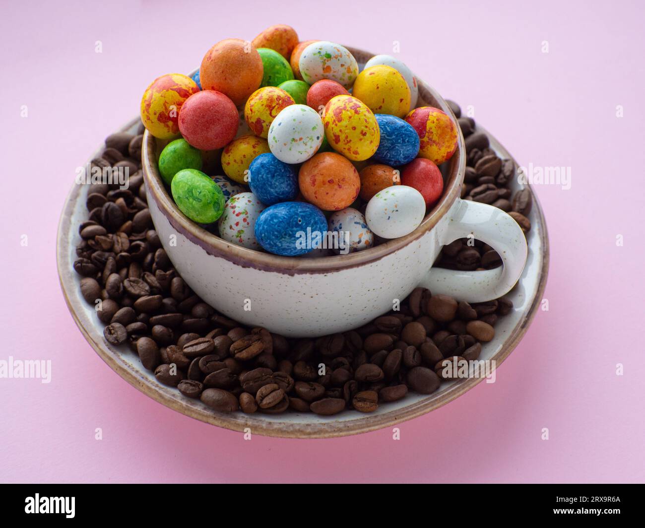 Composizione con piccole uova di pasqua al cioccolato in tazza circondata da chicchi di caffè tostati. Caffè pasquale. Tazza piena di uova colorate su un piatto wi Foto Stock