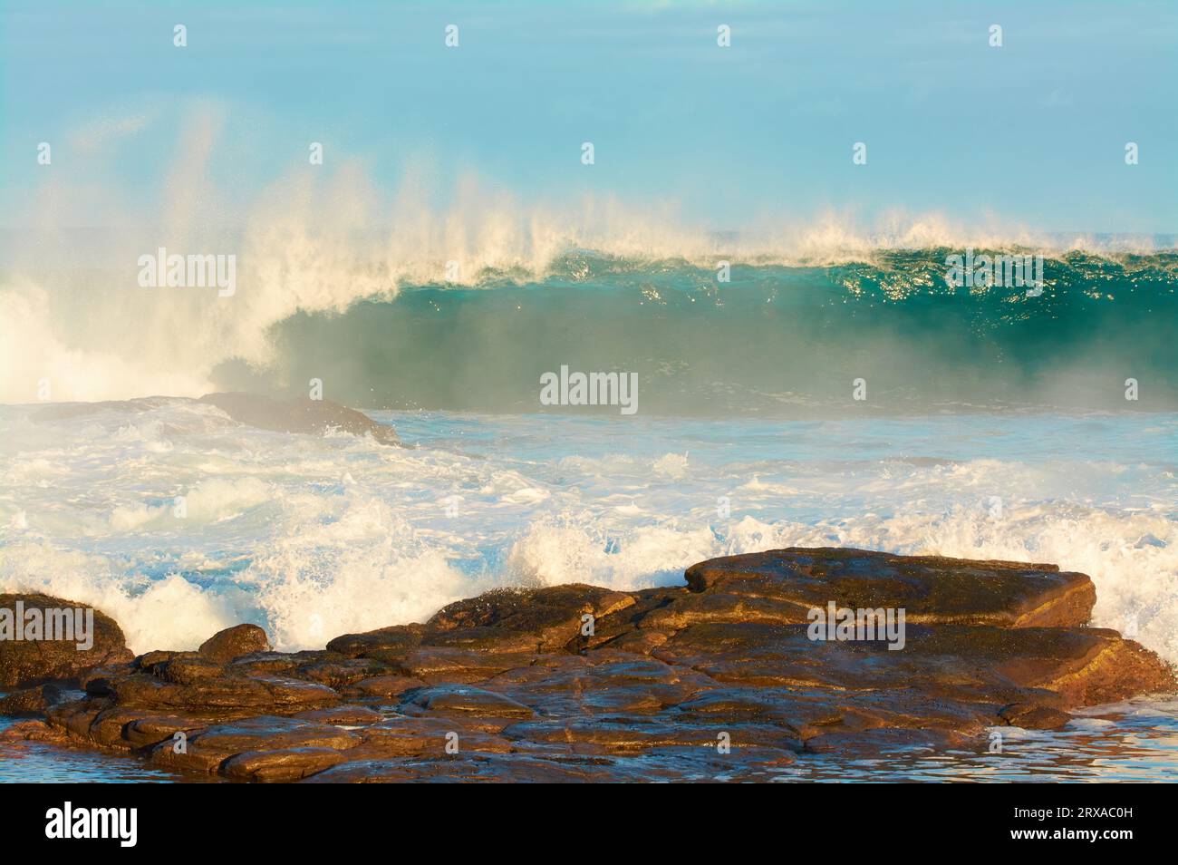 Una grande onda che si rompe all'alba con rocce di granito in primo piano, Prevelly Beach, regione di Margaret River, Australia Occidentale Foto Stock