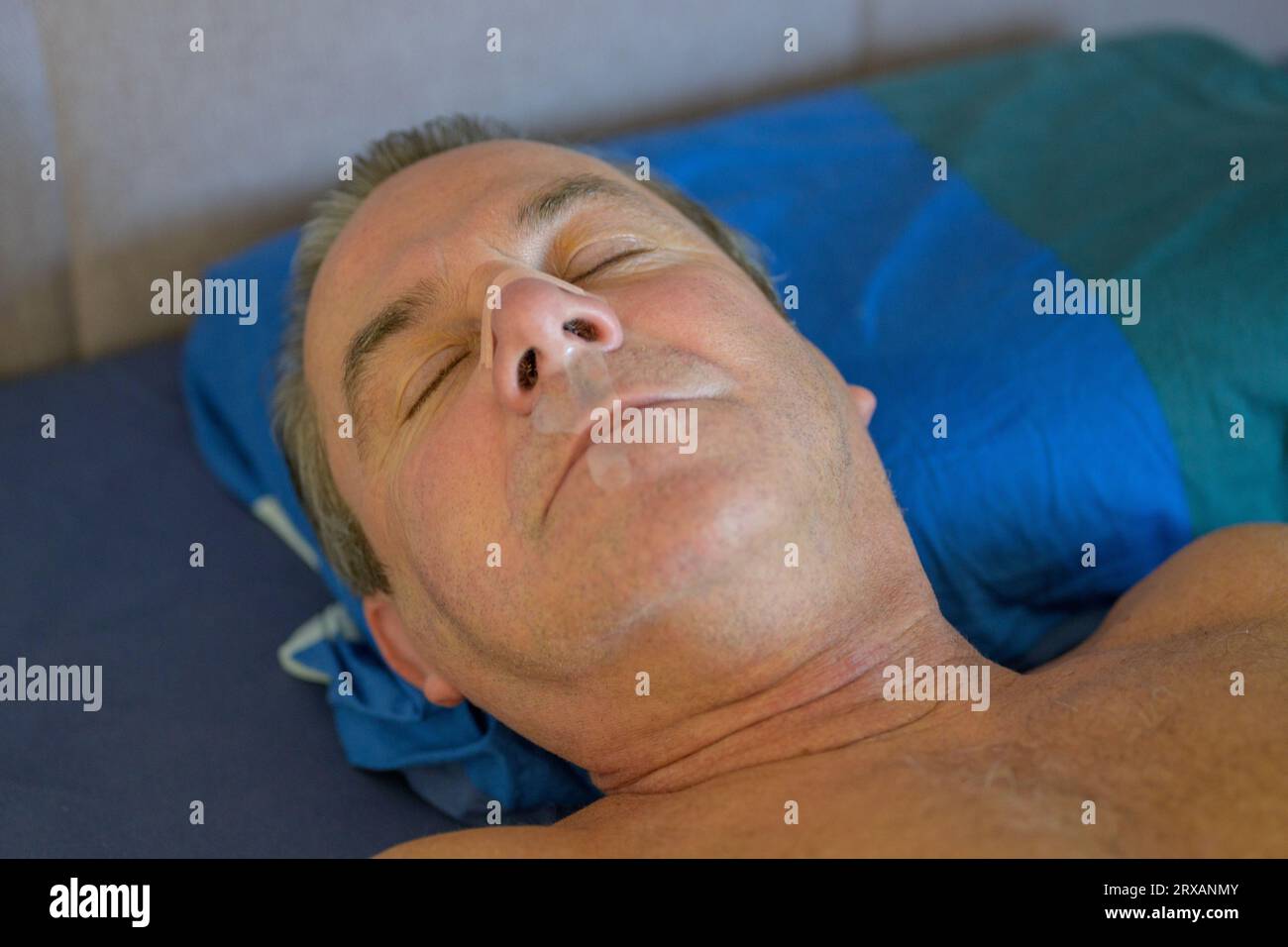 Primo piano di un uomo di mezza età addormentato con un nastro per il naso e un nastro per la bocca sdraiato nel letto Foto Stock