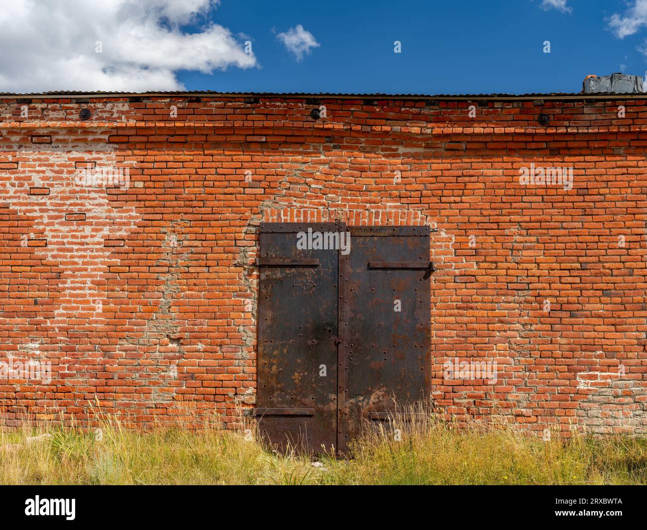 Edificio in mattoni abbandonato con una porta di metallo arrugginito Foto Stock