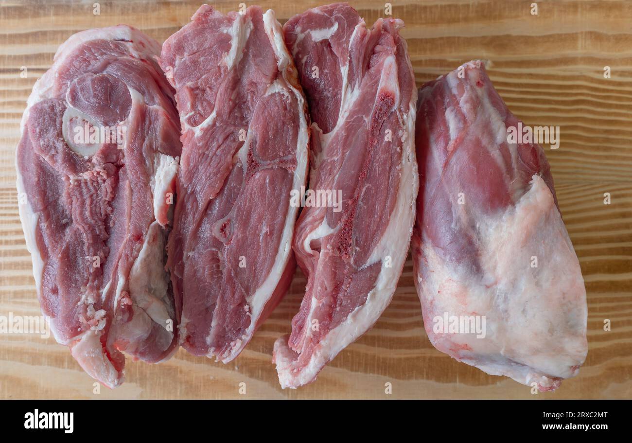 Una spalla di agnello è tagliata in quattro pezzi e avvolta in carta bianca su un tavolo di legno. Foto Stock