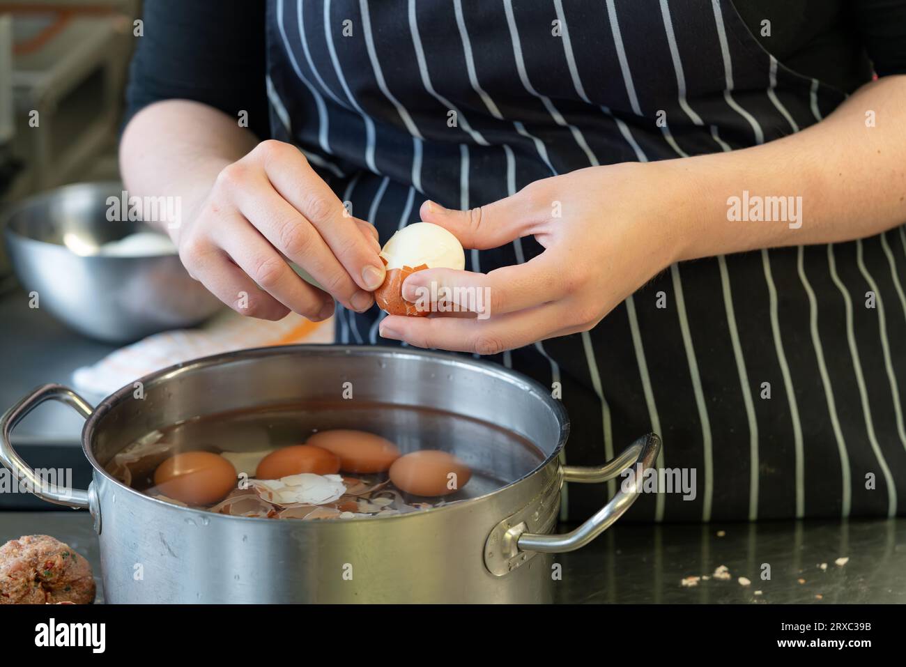 Una chef donna si vede sbucciare uova sode in cucina. Foto Stock