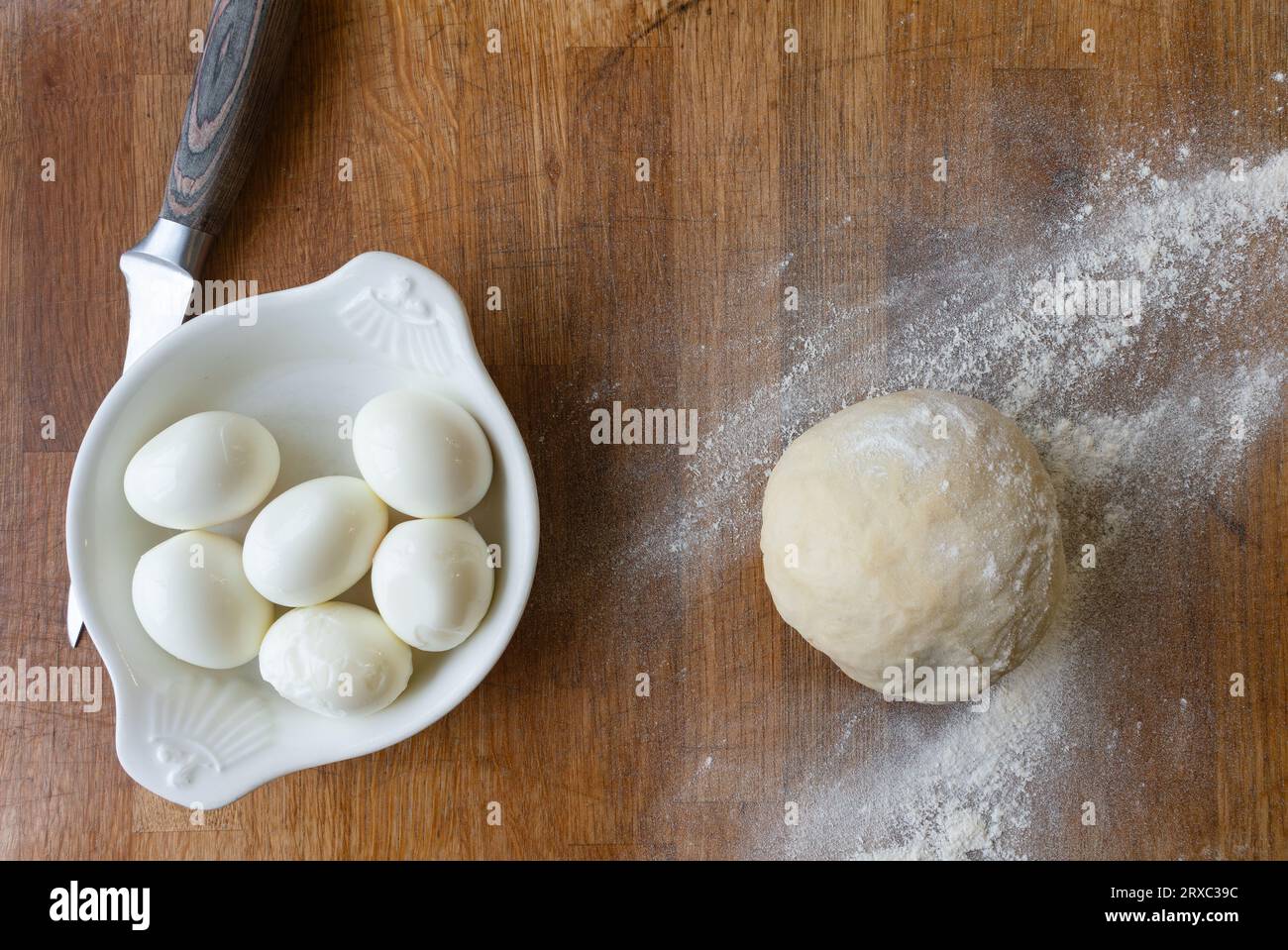 Un blocco di legno è allestito con uova di pasticceria e un coltello, tutti pronti per la preparazione di una torta di gala. Foto Stock