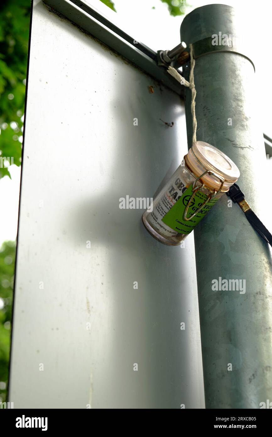 Luglio 2023 - Geocaching Containers dietro un cartello stradale nel Somerset rurale, in Inghilterra, Regno Unito. Foto Stock