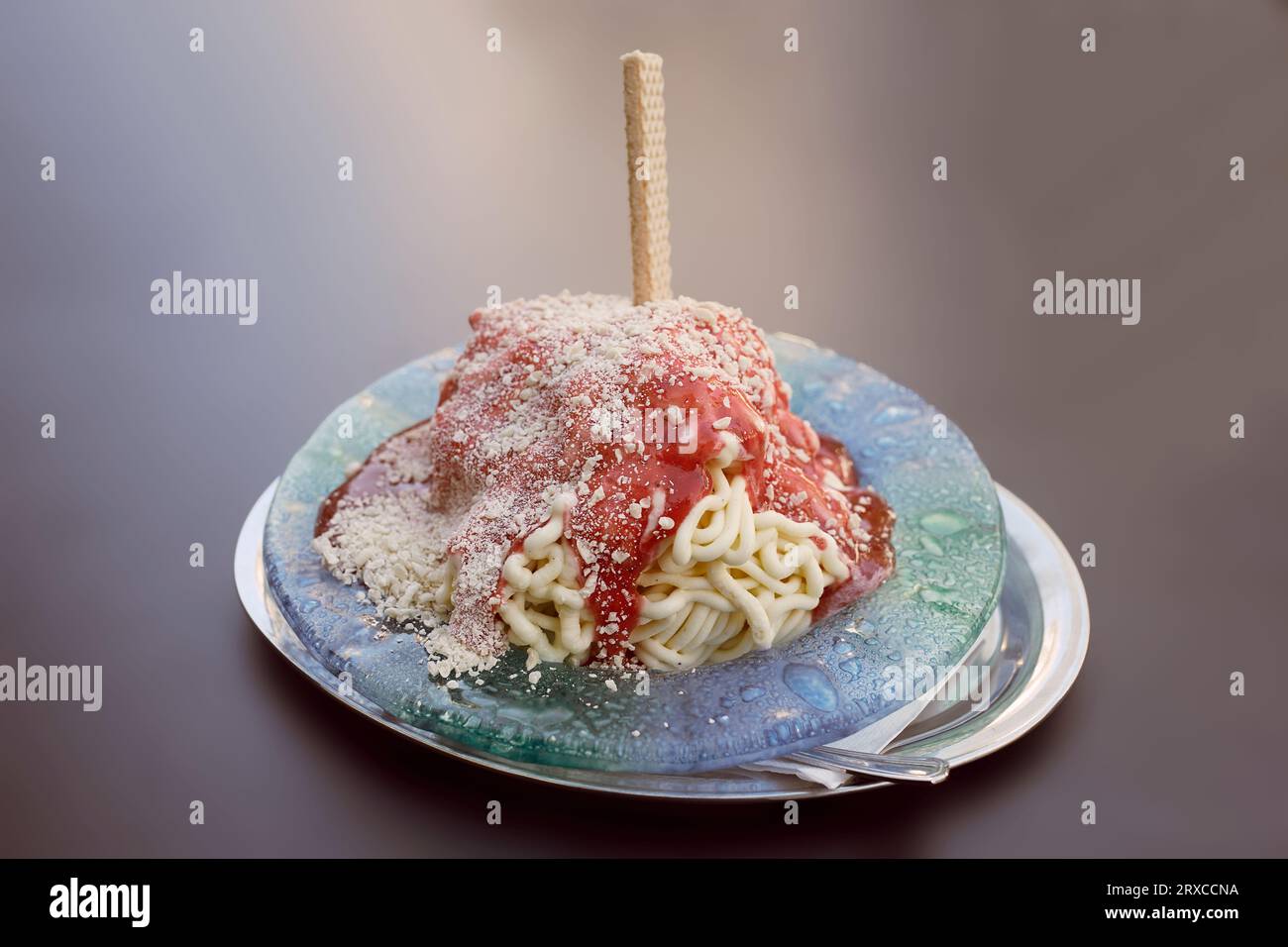 gelato agli spaghetti in un piatto, isolato su fondo marrone Foto Stock