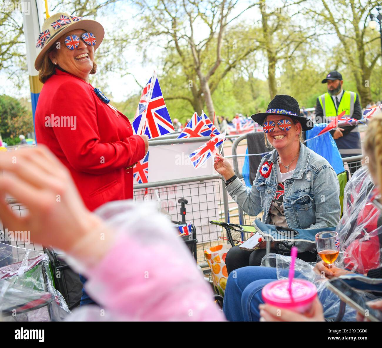 Due donne sorridono e festeggiano mentre campeggiano sul Mall London UK prima dell'incoronazione di re Carlo, vestita con occhiali Union Jack che sventolano le bandiere Foto Stock