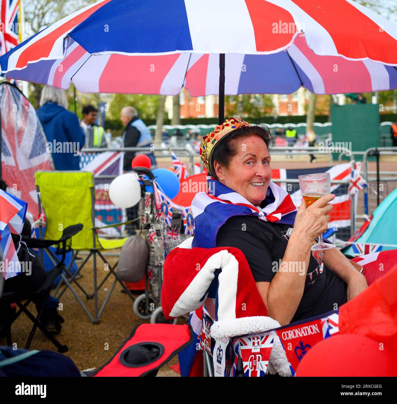 Una signora sorride alla telecamera vestita con Union Jack tenendo un drink in una posizione sicura nel centro commerciale di Londra Inghilterra per l'incoronazione di re Carlo Foto Stock