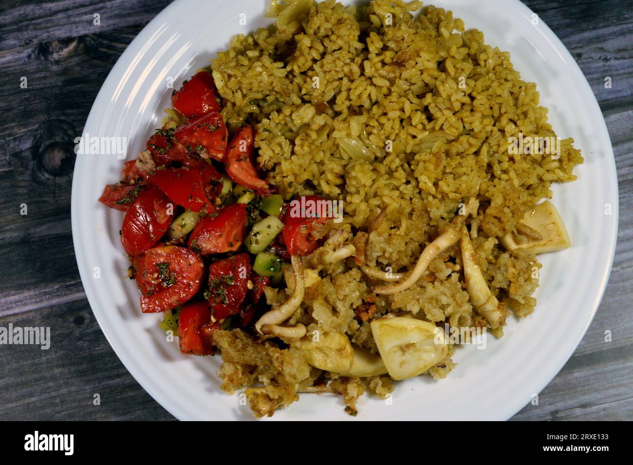 Un piatto di riso rosso caldo al vapore, insalata verde e calamari fritti, un mollusco dal corpo morbido allungato, occhi grandi, otto braccia e due tentacoli nel Foto Stock