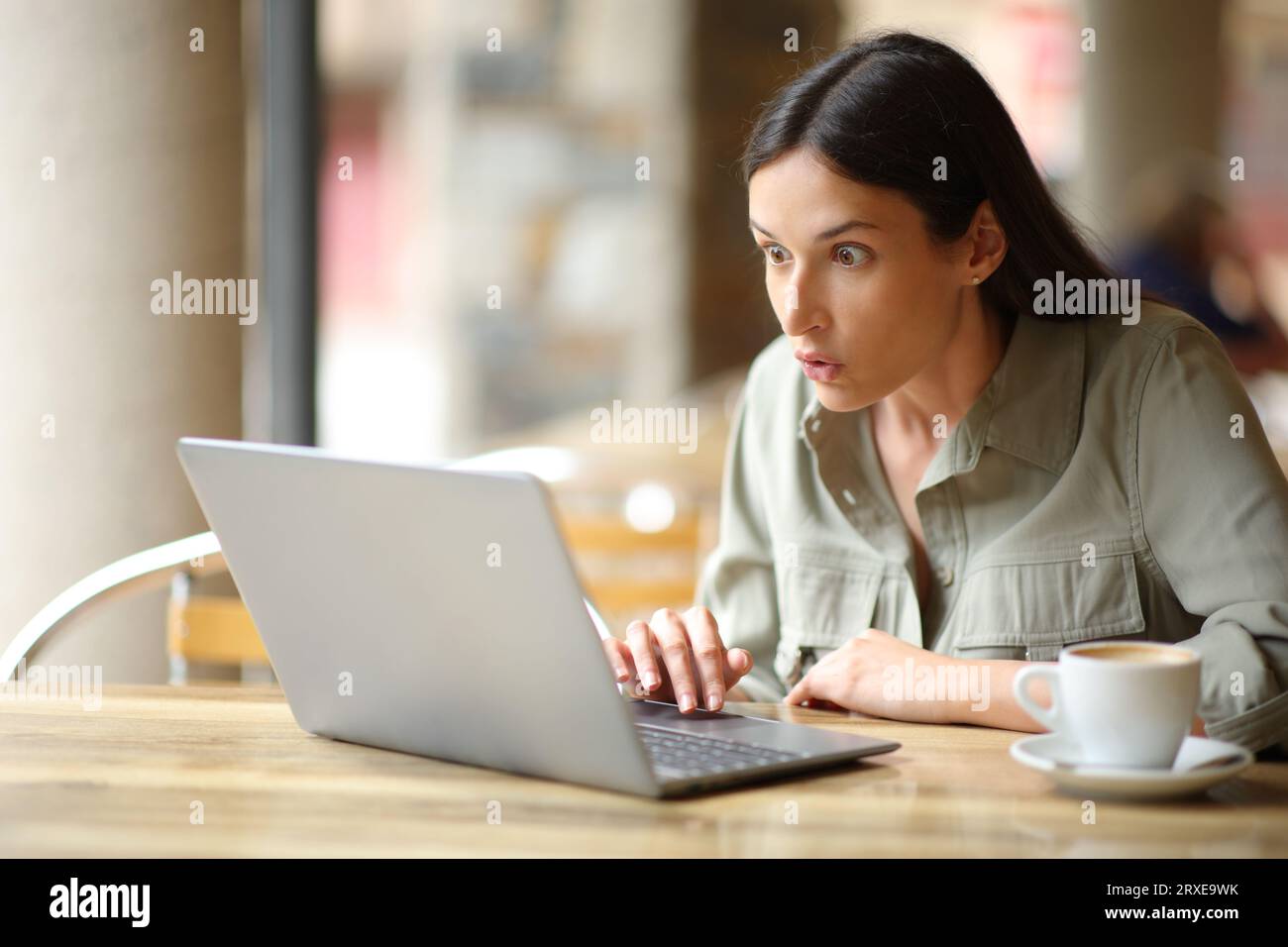 Una donna stupita che guarda contenuti sorprendenti su un notebook nella terrazza di un ristorante Foto Stock