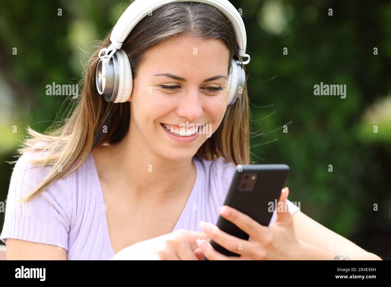 Adolescente felice che usa il cellulare e le cuffie in un parco Foto Stock