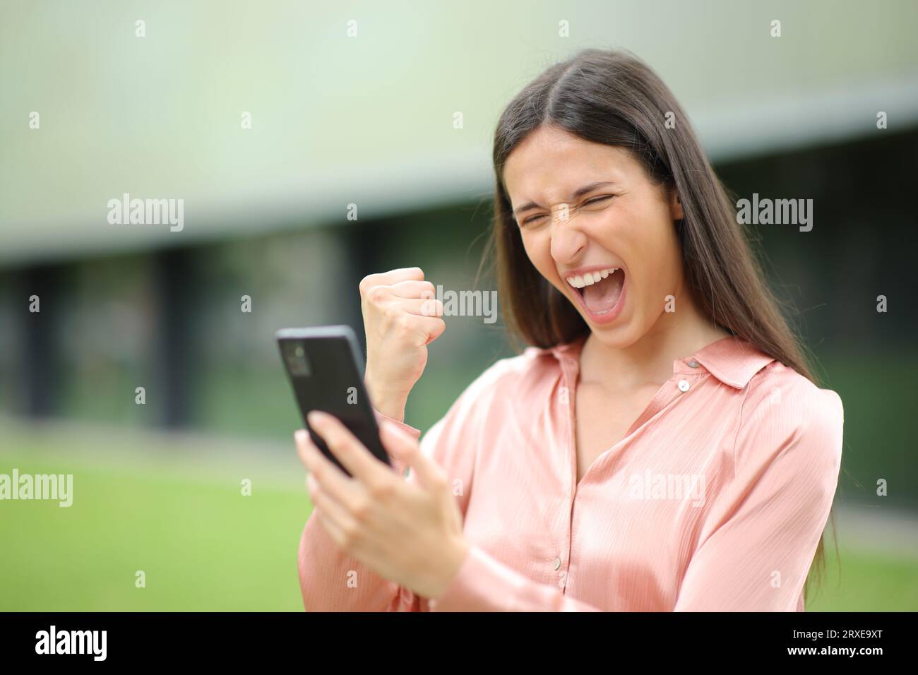 Una donna eccitata che cammina per strada sta controllando il telefono e festeggiando il successo Foto Stock