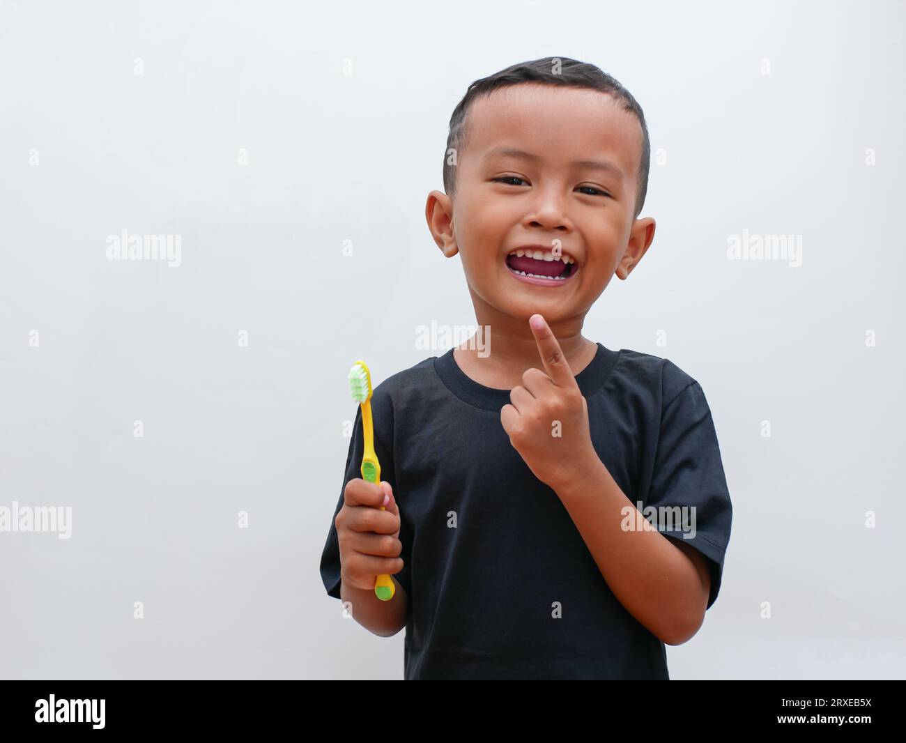 piccolo ragazzo asiatico che tiene uno spazzolino da denti sorridendo su sfondo bianco con spazio per la copia. concetto di salute dentale per bambini Foto Stock