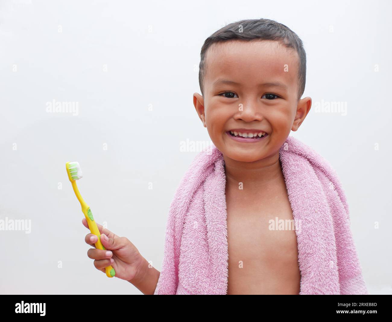piccolo ragazzo asiatico che tiene uno spazzolino da denti sorridendo su sfondo bianco con spazio per la copia. concetto di salute dentale per bambini Foto Stock