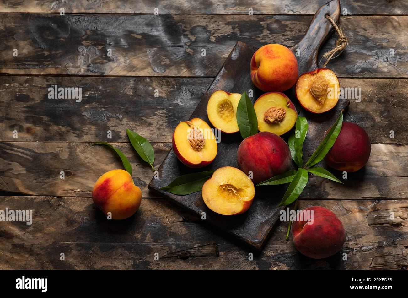Pesche rosse scure fresche mature con foglie su tagliere e tavolo in legno. Frutta intera e metà di deliziose pesche di arancia brillante e succulente in ingresso Foto Stock