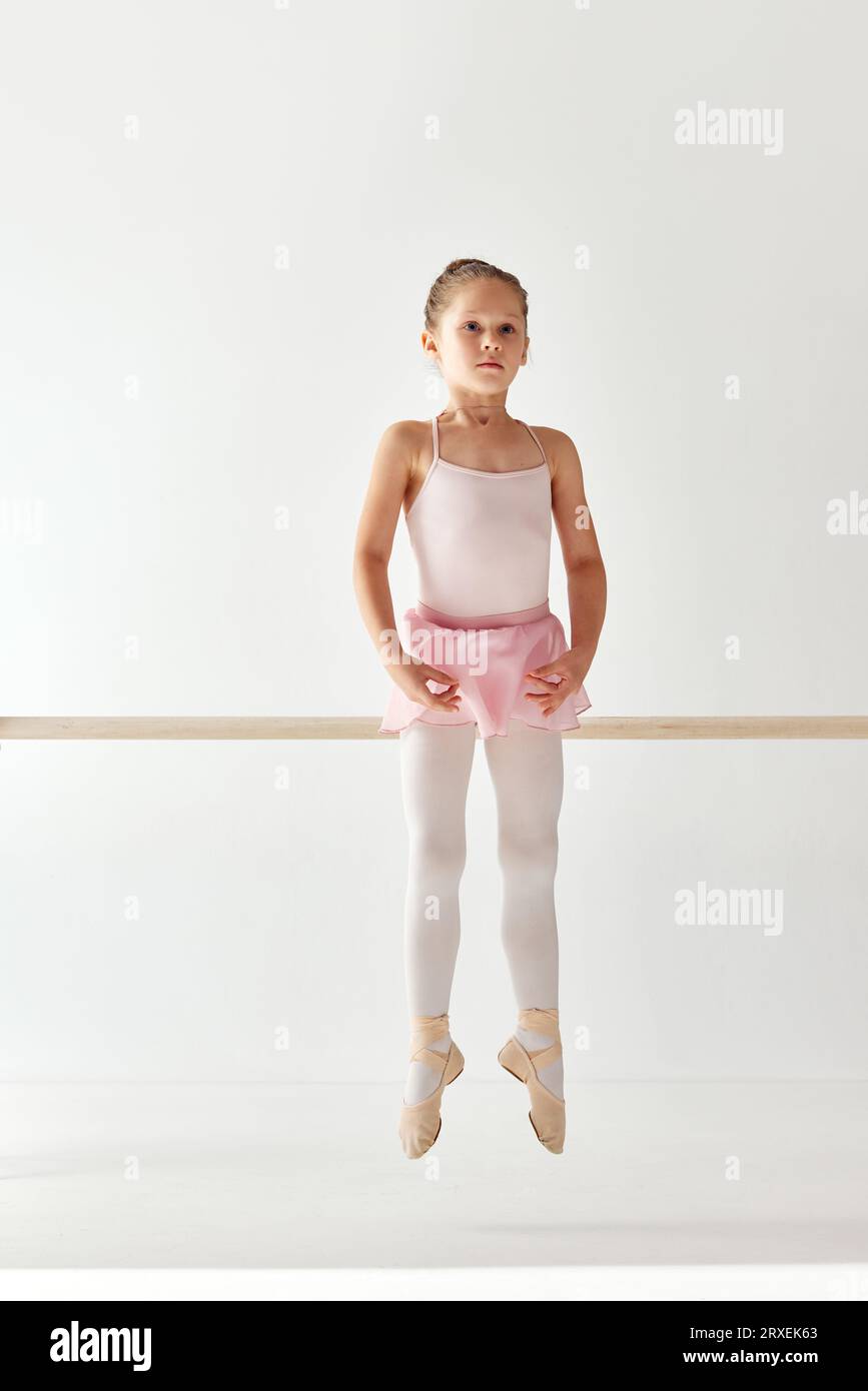 Ritratto retrovisivo di una piccola adorabile ballerina con abito da ballo in tutu rosa su pointe che posa ed esegue elementi di danza. Lezioni di istruzione Foto Stock