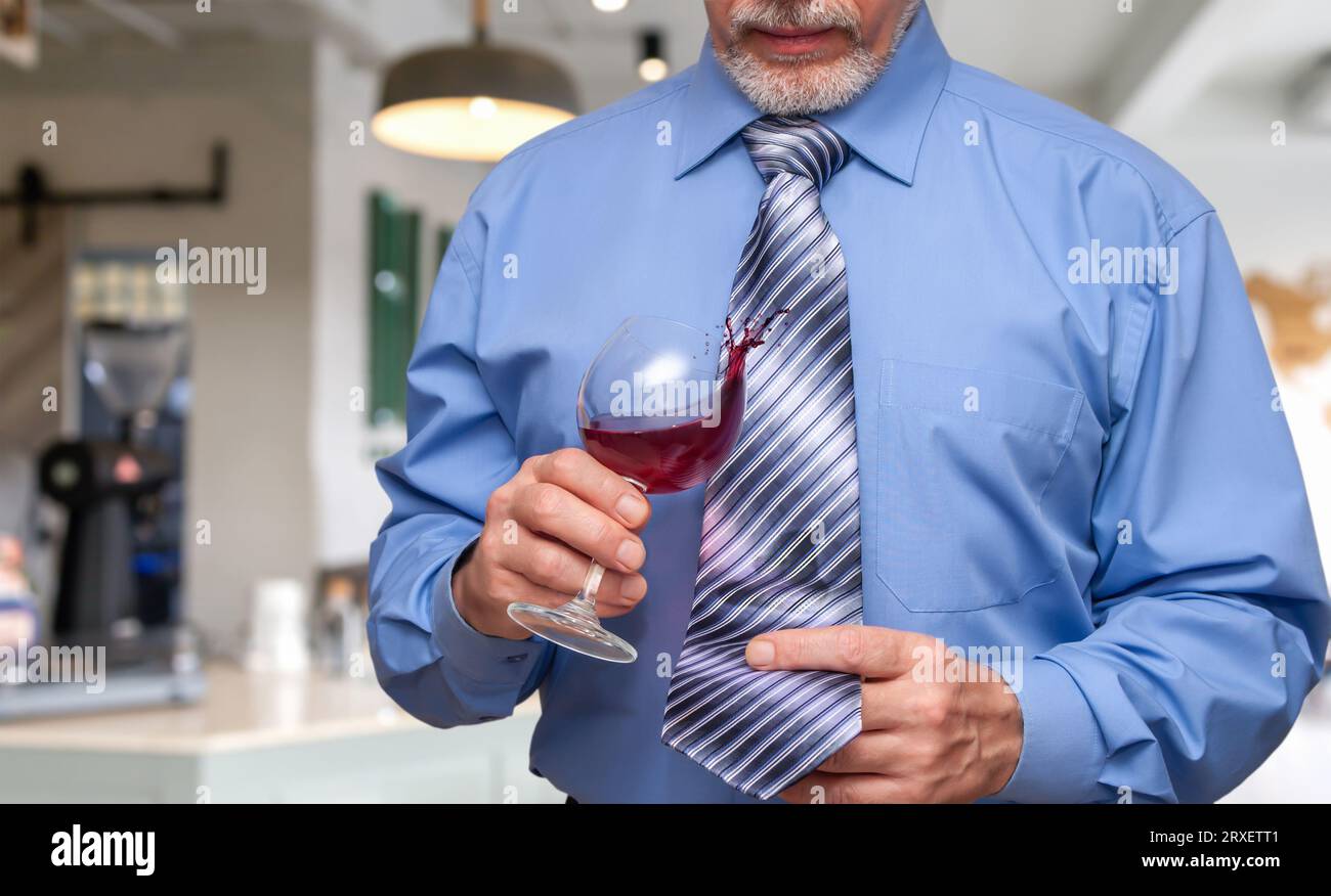 Un uomo che tiene un bicchiere di vino in mano e lascia che un po' di vite goccioli sulla sua cravatta. Foto Stock