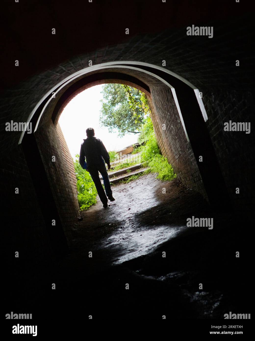 Vista posteriore di una persona che cammina attraverso un tunnel buio. Foto Stock