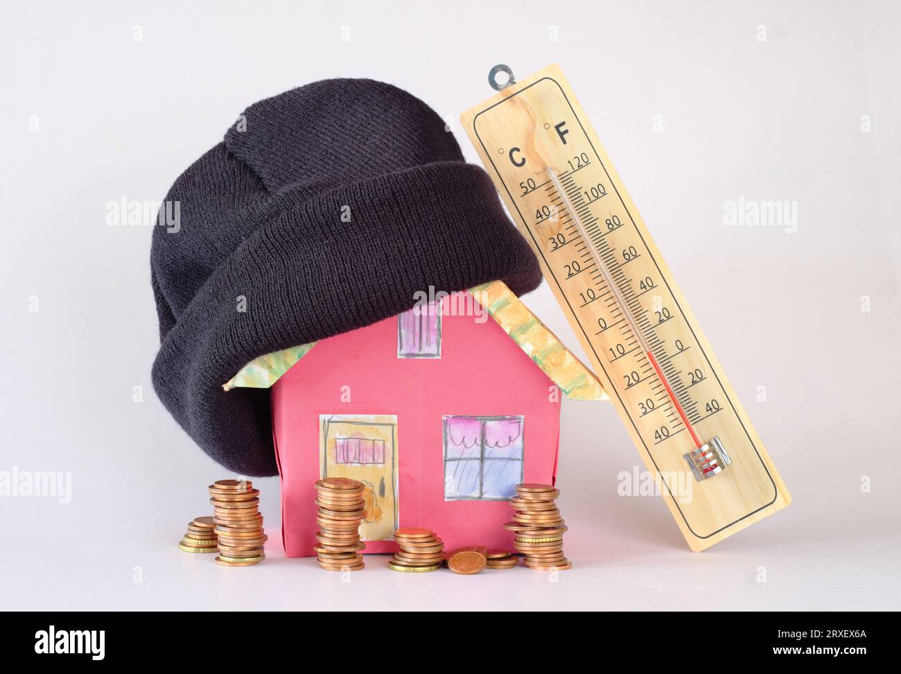Modellare casa con cappello invernale, pile di denaro e termometro. Aumento dei costi di riscaldamento, isolamento termico e prezzi dell'energia a causa della carenza di gas di riscaldamento, Foto Stock