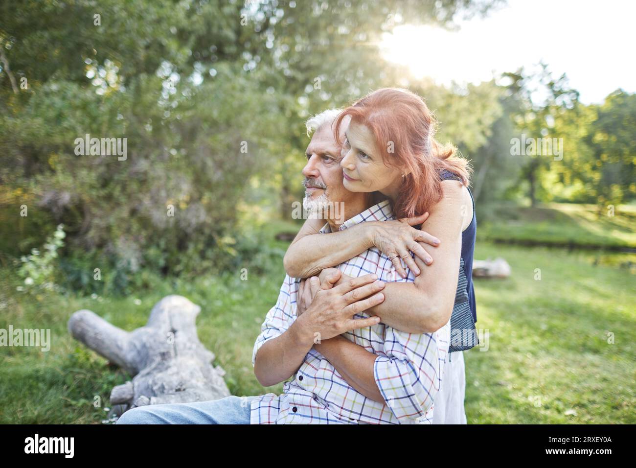 donna anziana che abbraccia un uomo dai capelli grigi seduto nel parco Foto Stock