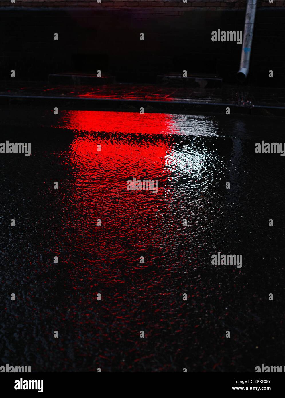Il riflesso della luce rossa nell'asfalto bagnato di notte. Luce anabbagliante. Luci rosse Foto Stock