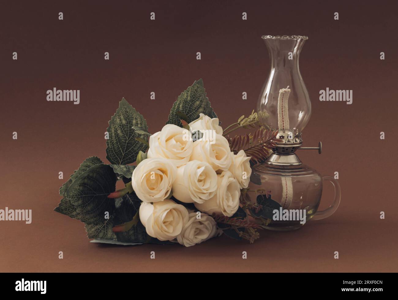 Classico bouquet di rose bianche e vecchia lampada a gas su sfondo marrone. Decorazioni in stile vintage. Foto Stock