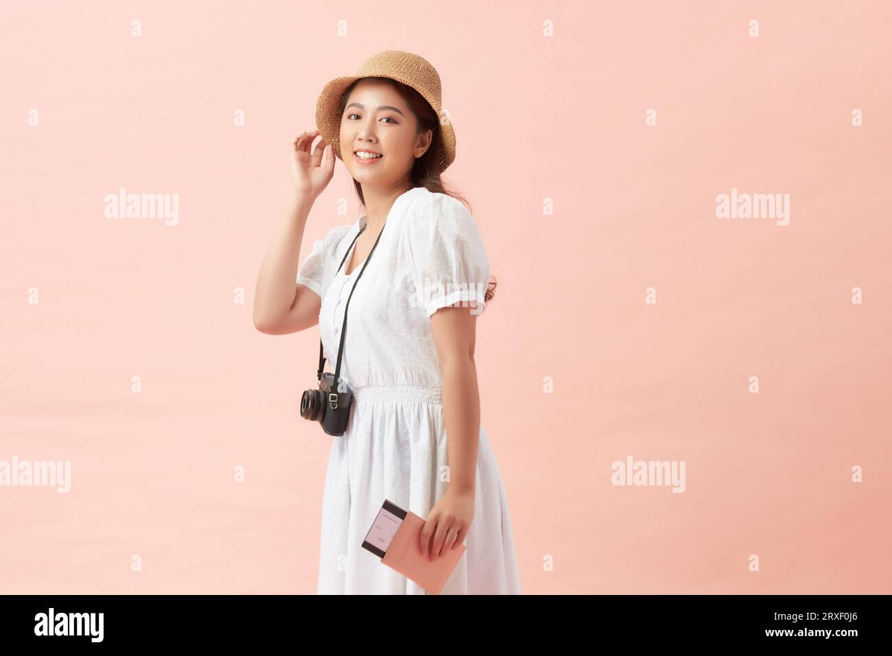 Una donna turistica felice che indossa un cappello con i biglietti per la fotocamera sembra isolata su sfondo rosa Foto Stock