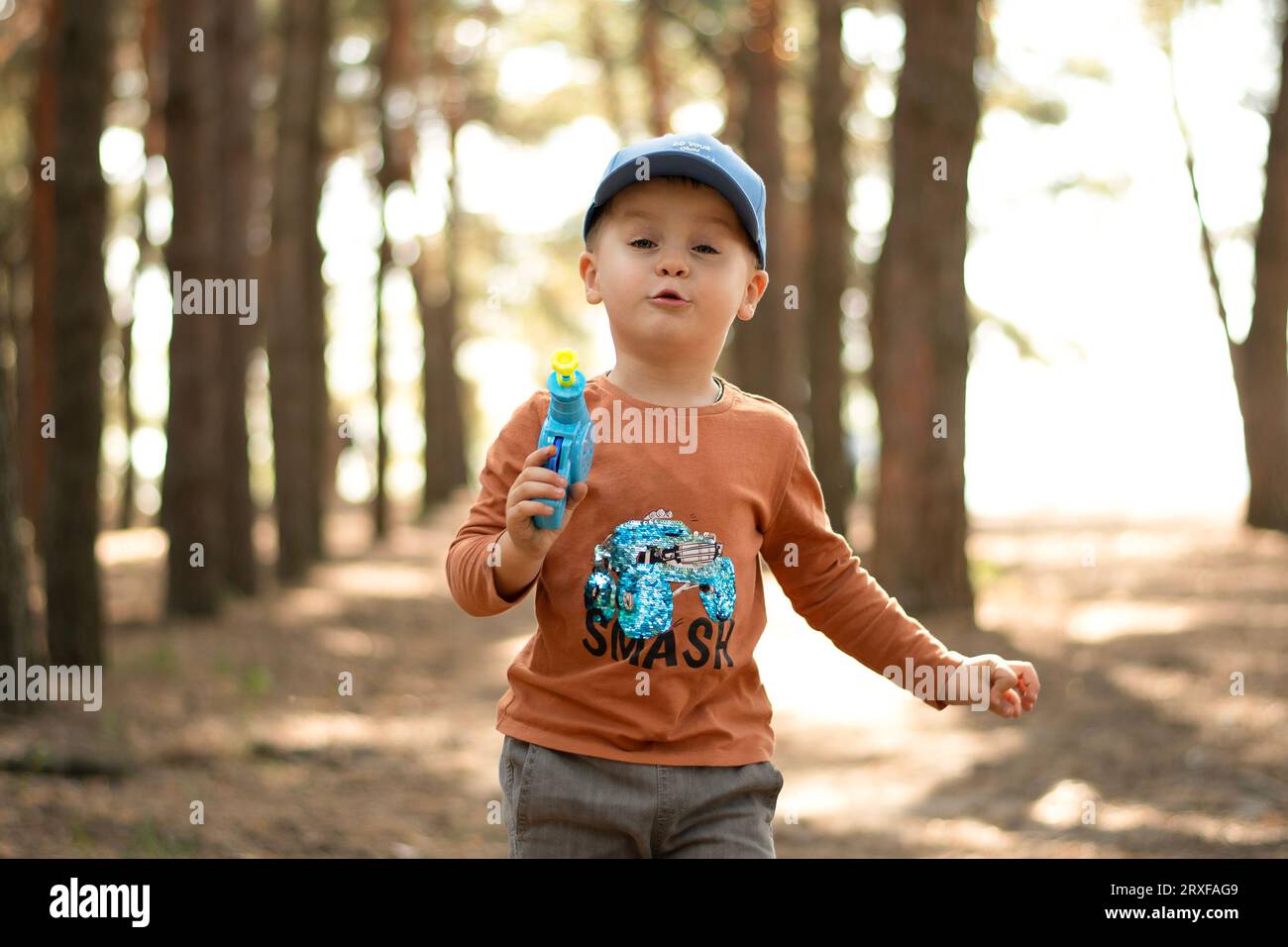 Bambini. Un piccolo ragazzo bello ed emotivo con un berretto blu e una giacca rossa gioca con le bolle di sapone nell'aria fresca della foresta. Foto Stock