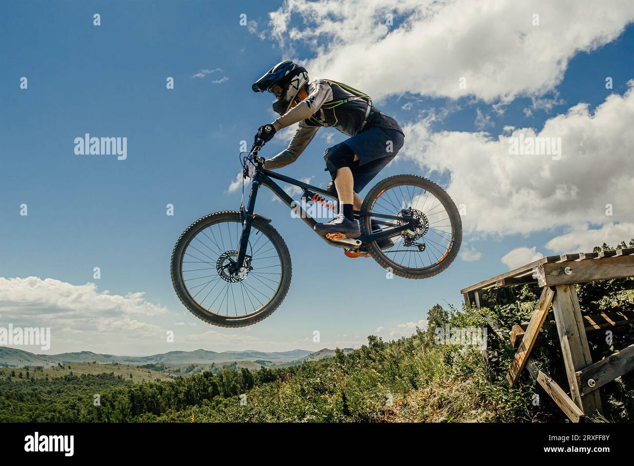 atleta mountain biker saltare giù giù in volo. sullo sfondo del cielo azzurro e delle montagne Foto Stock