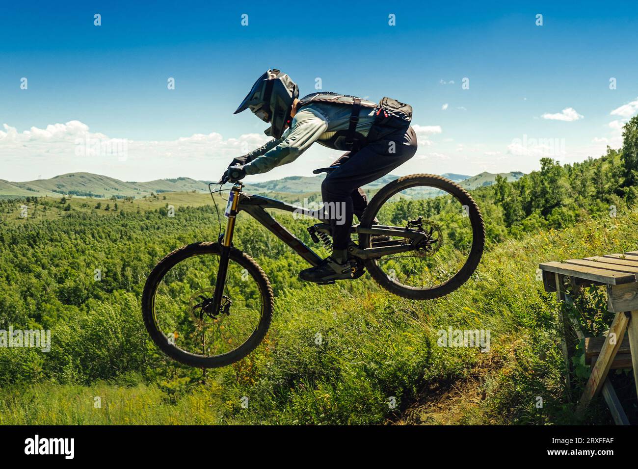 l'atleta di mountainbiker salta giù in volo. sullo sfondo delle montagne nella verde foresta Foto Stock