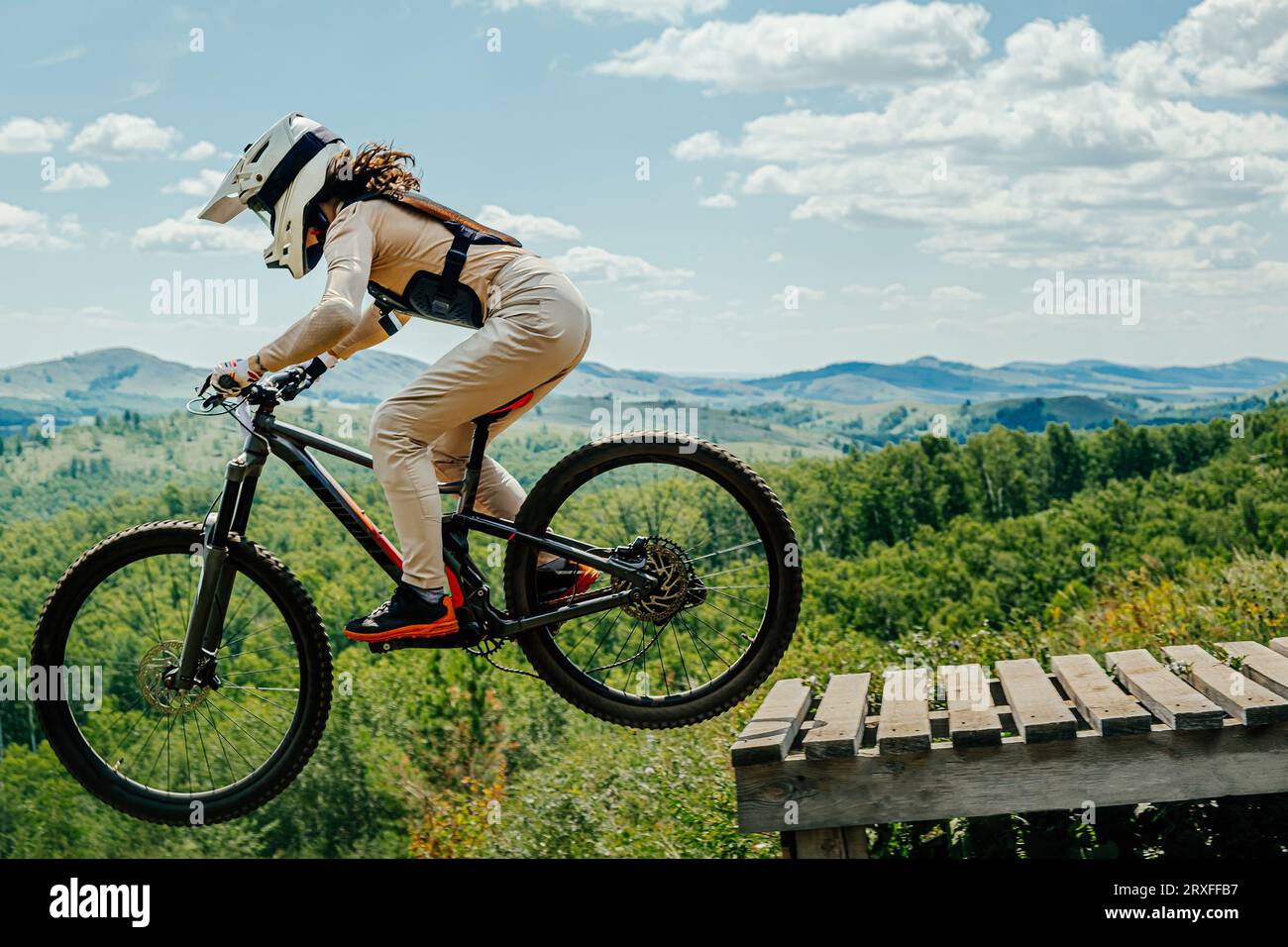 atleta femminile di mountainbiker saltare giù in discesa in volo. sullo sfondo delle montagne nella foresta Foto Stock