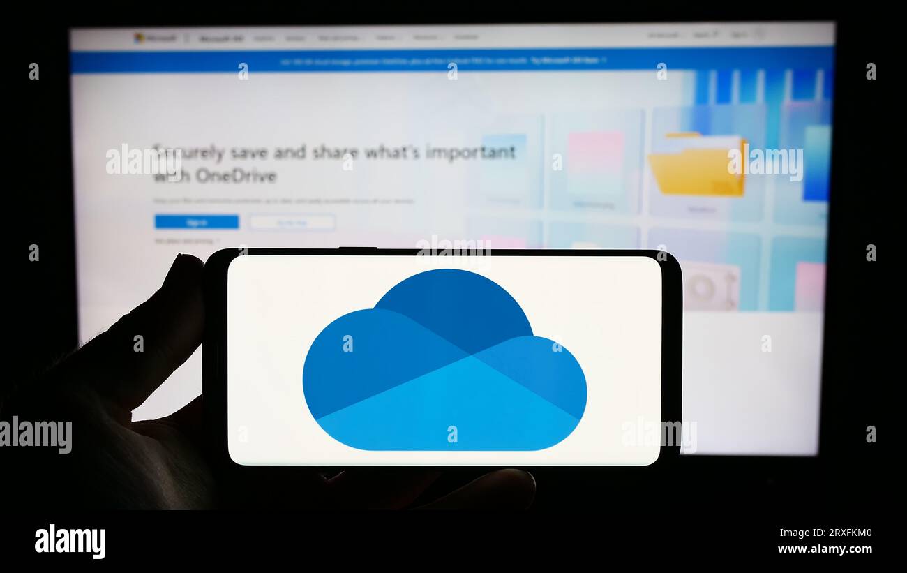 Persona che possiede uno smartphone con il logo del servizio di hosting file Microsoft OneDrive sullo schermo davanti al sito Web. Concentrarsi sul display del telefono. Foto Stock
