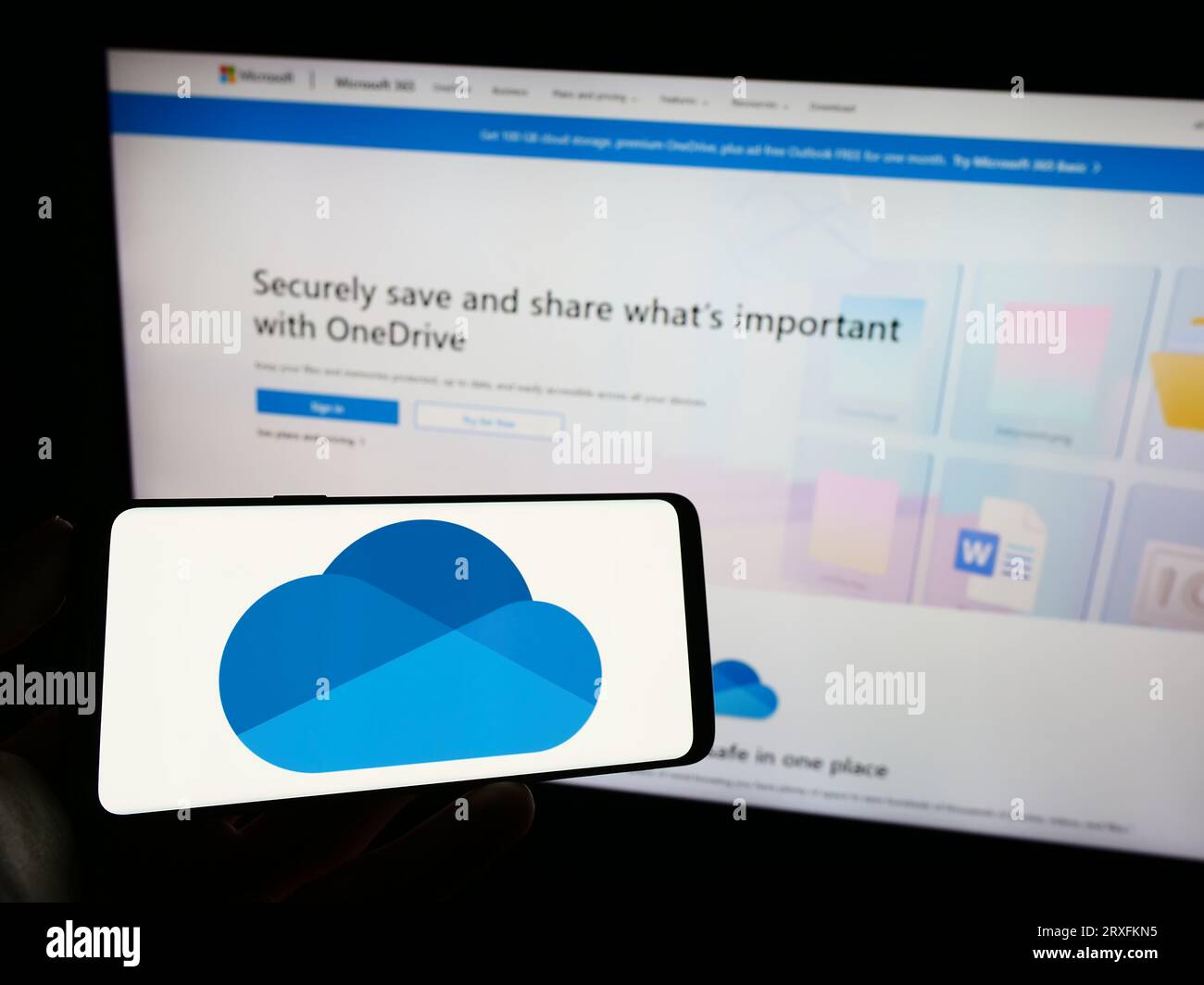 Persona che possiede il cellulare con il logo del servizio di hosting file Microsoft OneDrive sullo schermo davanti alla pagina Web aziendale. Concentrarsi sul display del telefono. Foto Stock