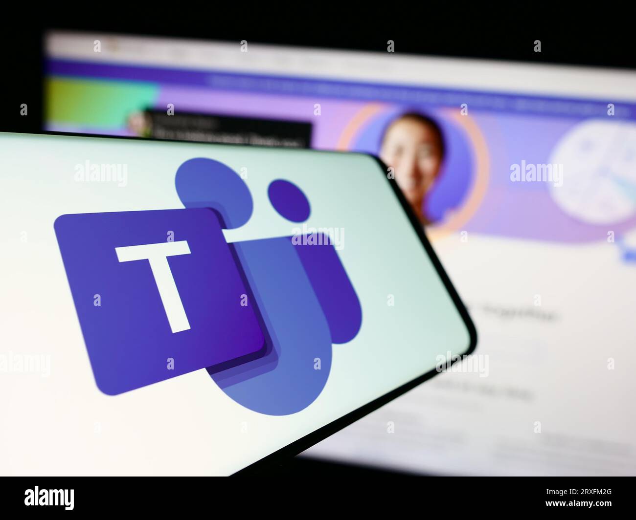 Cellulare con logo della piattaforma di comunicazione aziendale Microsoft Teams sullo schermo davanti al sito Web. Mettere a fuoco il display centrale sinistro del telefono. Foto Stock