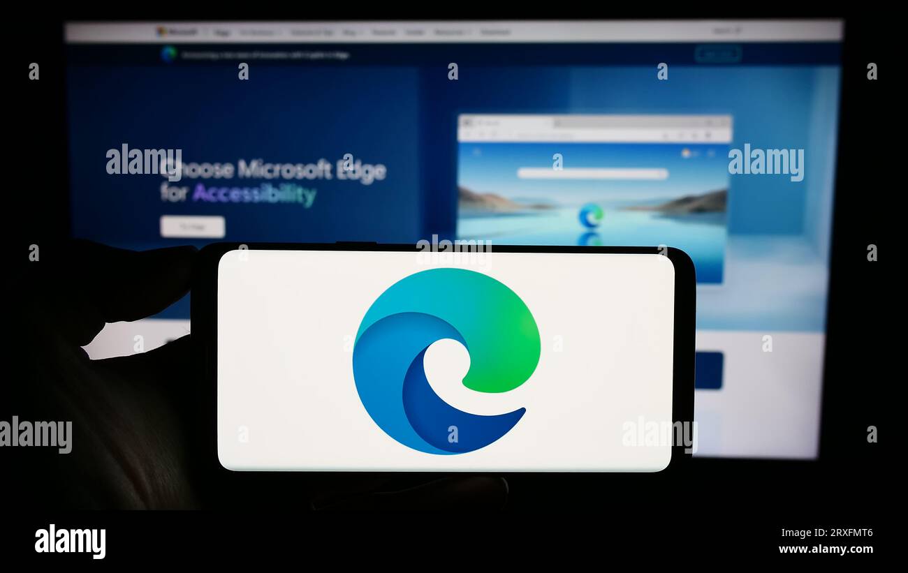 Persona che possiede il cellulare con il logo del browser Web Microsoft Edge sullo schermo davanti alla pagina Web dell'azienda. Concentrarsi sul display del telefono. Foto Stock