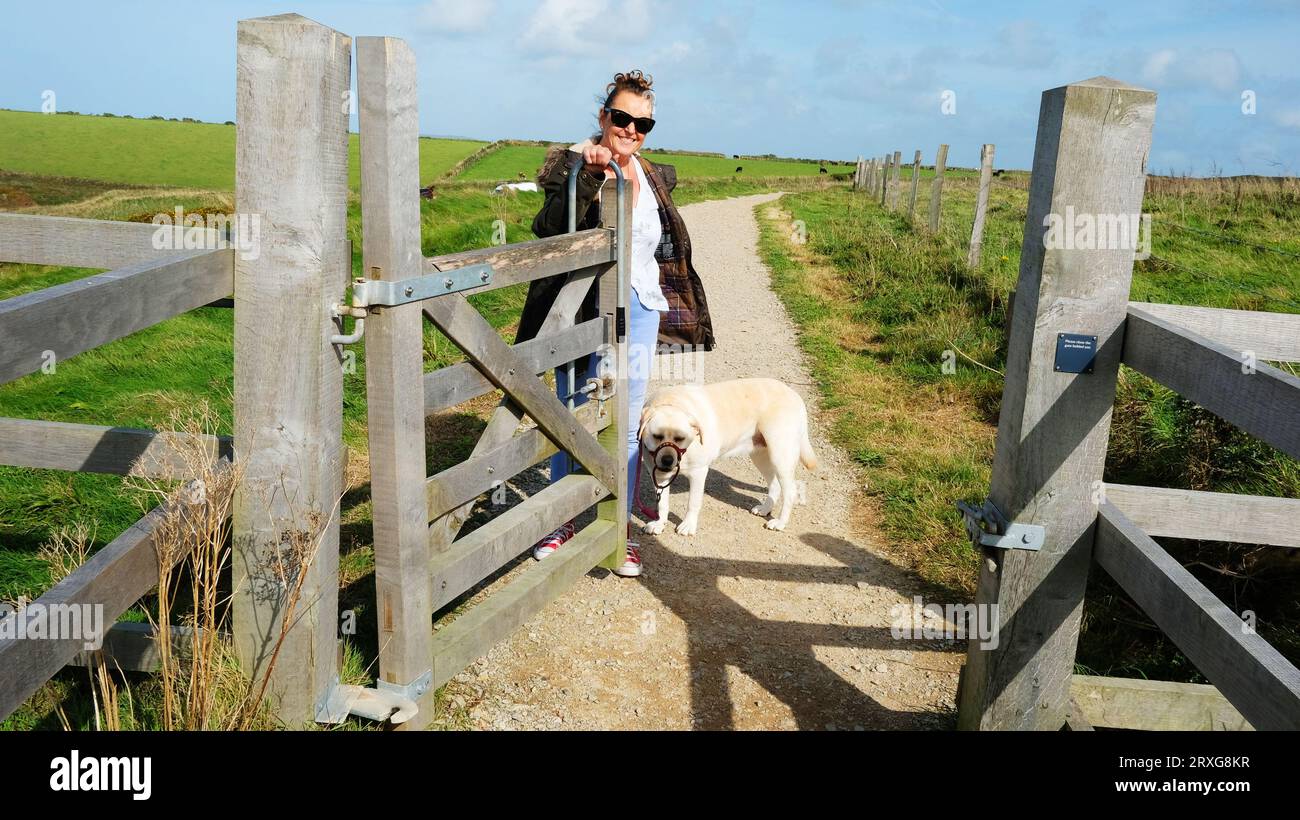Passerella per cani femmina che apre il cancello per consentire il passaggio di altre persone, Cornwall, Regno Unito - John Gollop Foto Stock