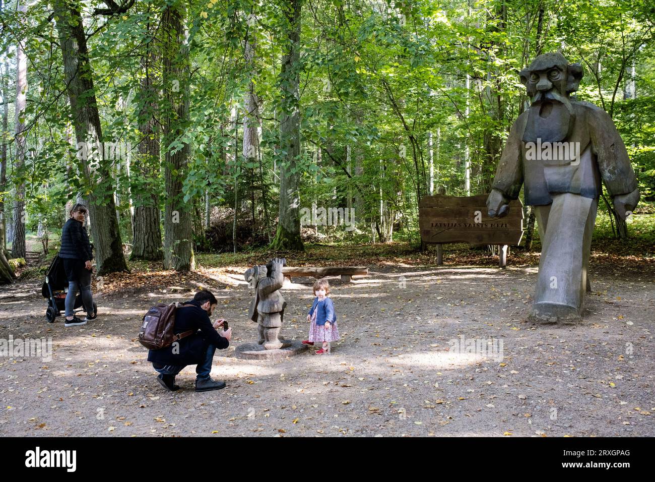 Famiglia vicino alle sculture lignee raffiguranti i personaggi fiabeschi delle opere scritte da Anna Brigadere, Parco naturale di Tērvete, Lettonia Foto Stock