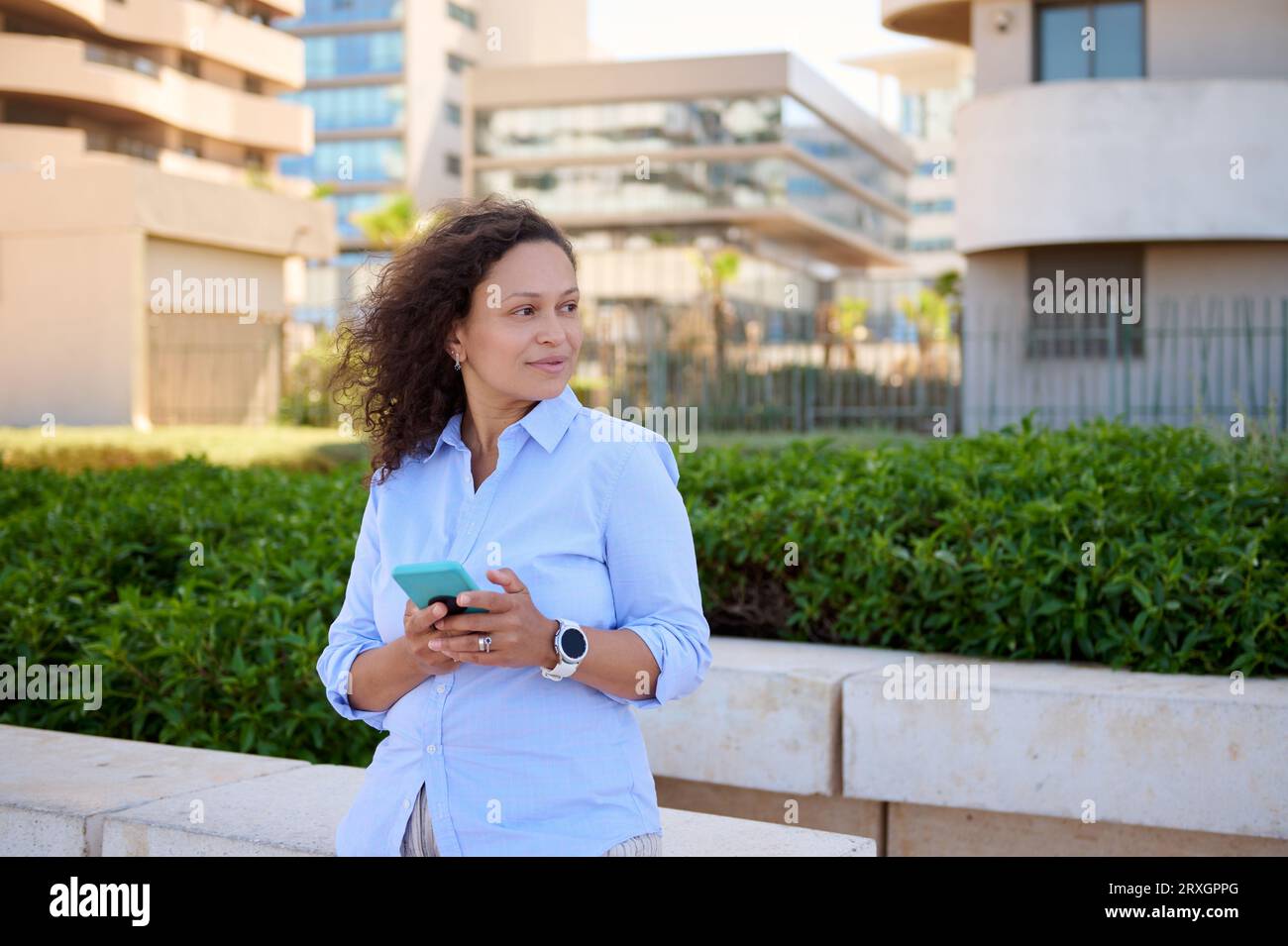 Autentico ritratto di una donna latinoamericana sicura di sé, imprenditrice 35-39 anni in camicia casual blu, sorridente guardando da parte, in piedi nella corta Foto Stock