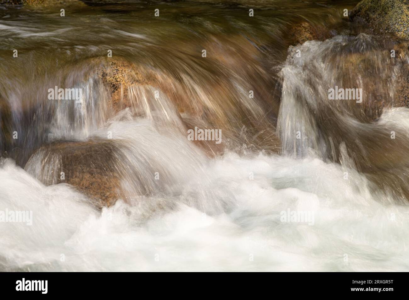 Ruscello di montagna che si schianta sulle rocce del fiume con acqua bianca e pietre di tonalità marrone in primo piano Foto Stock
