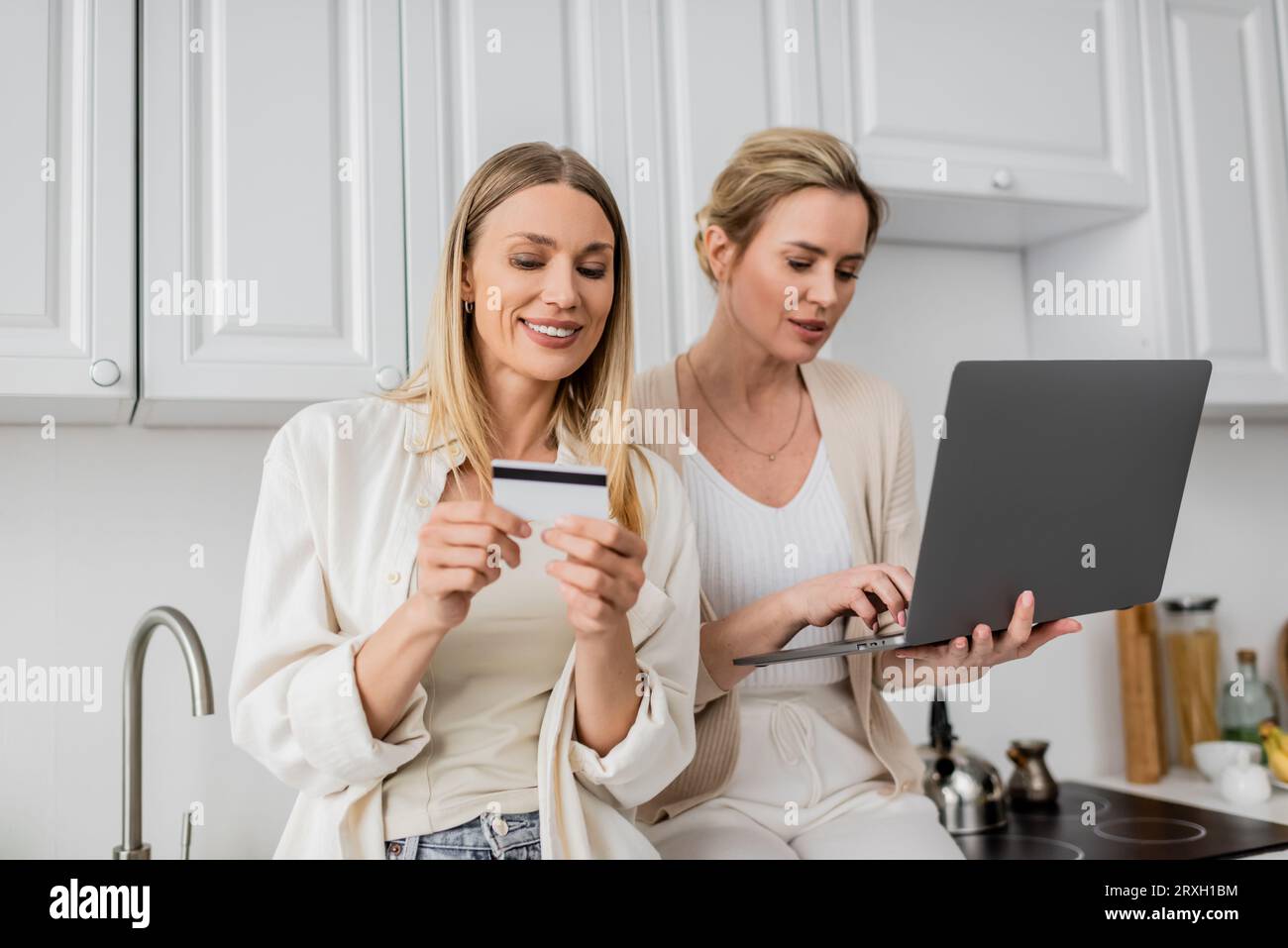 belle sorelle in un elegante stile pastello con carta di credito e computer portatile e un legame familiare Foto Stock