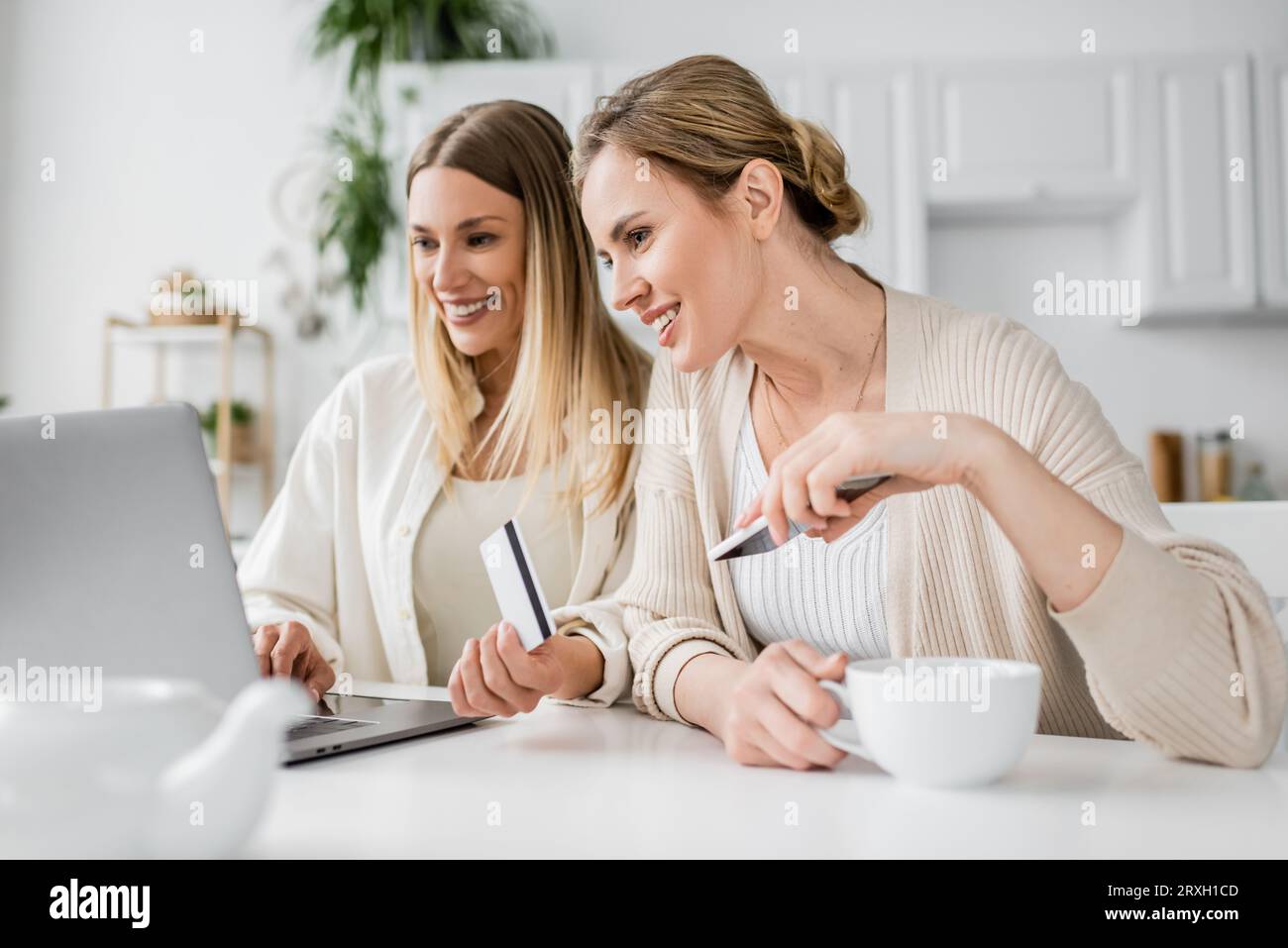 due bellissime sorelle bionde in un abbigliamento alla moda con carta di credito e una tazza di tè che guardano il computer portatile Foto Stock