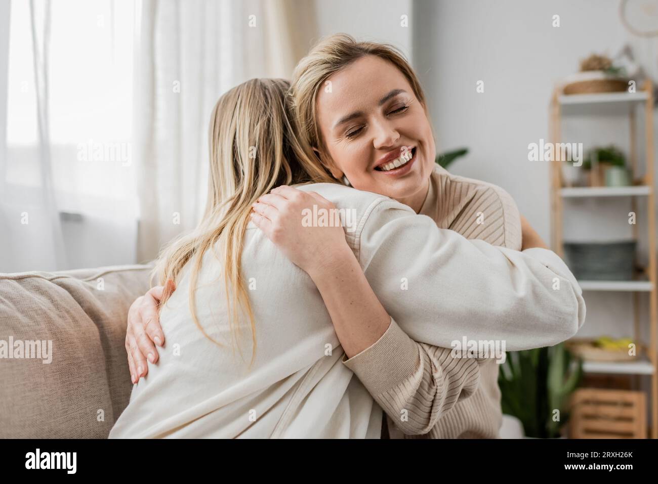 due sorelle bionde in un bell'abbigliamento informale abbracciano il divano con gli occhi chiusi, legando la famiglia Foto Stock