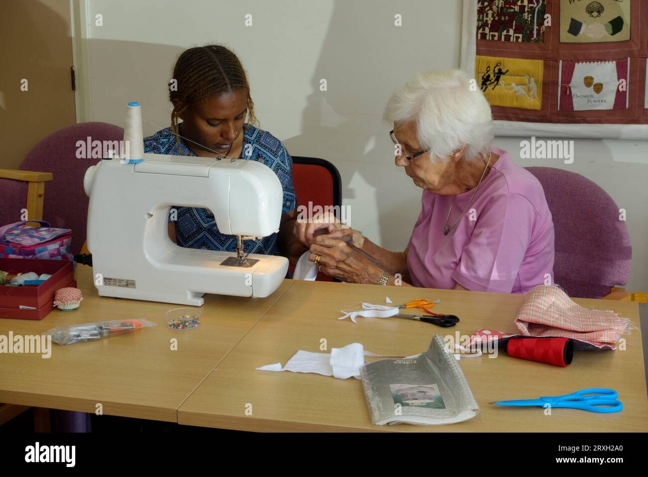Eldlerly bianca Europena donna inglese che insegna ai rifugiati etiopi come usare una macchina da cucire Regno Unito Foto Stock