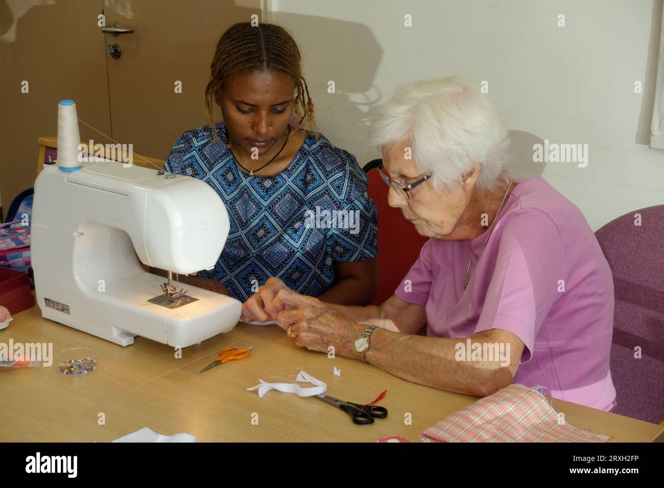 Eldlerly bianca Europena donna inglese che insegna ai rifugiati etiopi come usare una macchina da cucire Regno Unito Foto Stock